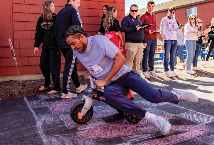 Miles Hester ’24 crosses a chalk drawn finish line on a trike with fellow student onlookers.