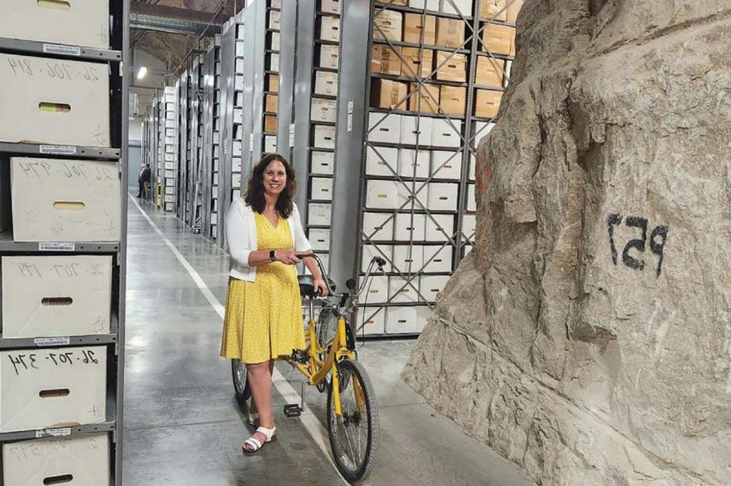 Colleen Shogan surrounded by files at the National Archives, beside a bicycle